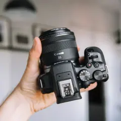 Dłoń trzyma aparat Canon z obiektywem 35mm. Zastanawiasz się, jakie aparaty fotograficzne wybrać? Ten model to świetny wybór.