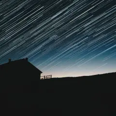 Sylwetka domu na tle nieba z długimi smugami gwiazd.