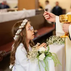 Dziewczynka w wianku przyjmuje komunię. Zastanawiasz się, ile kosztuje fotograf na komunie?