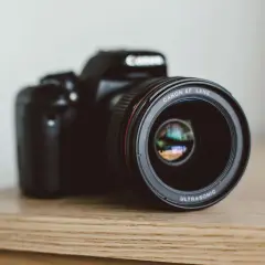 Czarna lustrzanka Canon z obiektywem EF LENS ULTRASONIC na drewnianym blacie.