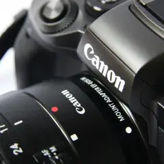 Zbliżenie na czarny aparat Canon z obiektywem, widoczne logo Canon i pokrętło trybów.