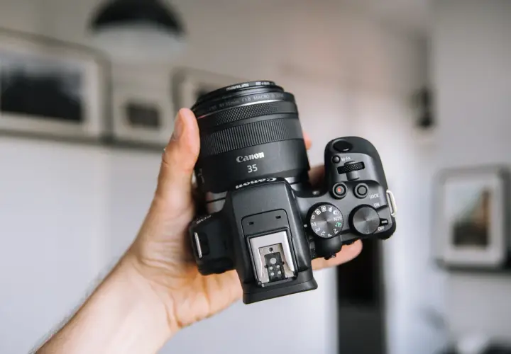 Dłoń trzyma aparat Canon z obiektywem 35mm. Zastanawiasz się, jakie aparaty fotograficzne wybrać? Ten model to świetny wybór.
