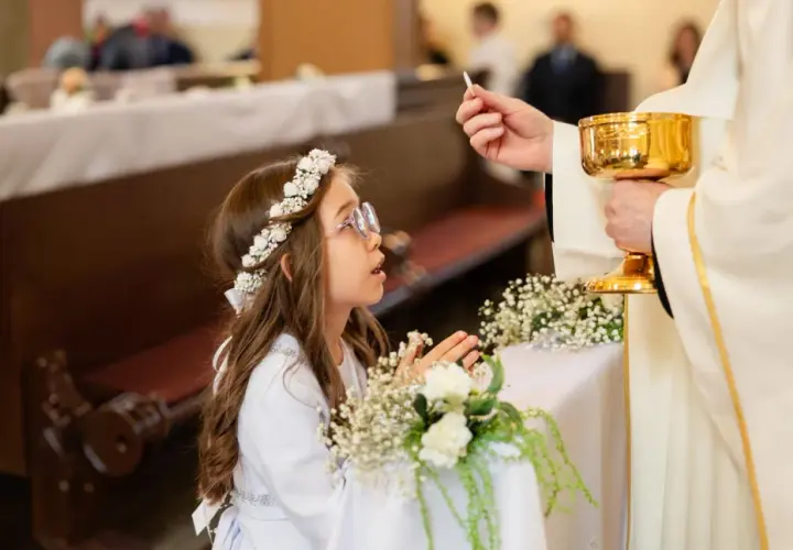 Dziewczynka w wianku przyjmuje komunię. Zastanawiasz się, ile kosztuje fotograf na komunie?