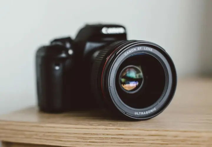 Czarna lustrzanka Canon z obiektywem EF LENS ULTRASONIC na drewnianym blacie.