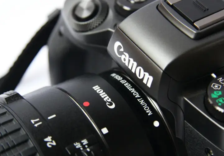 Zbliżenie na czarny aparat Canon z obiektywem, widoczne logo Canon i pokrętło trybów.