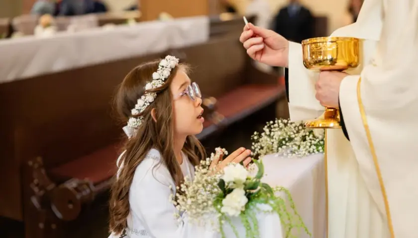 Dziewczynka w wianku przyjmuje komunię. Zastanawiasz się, ile kosztuje fotograf na komunie?