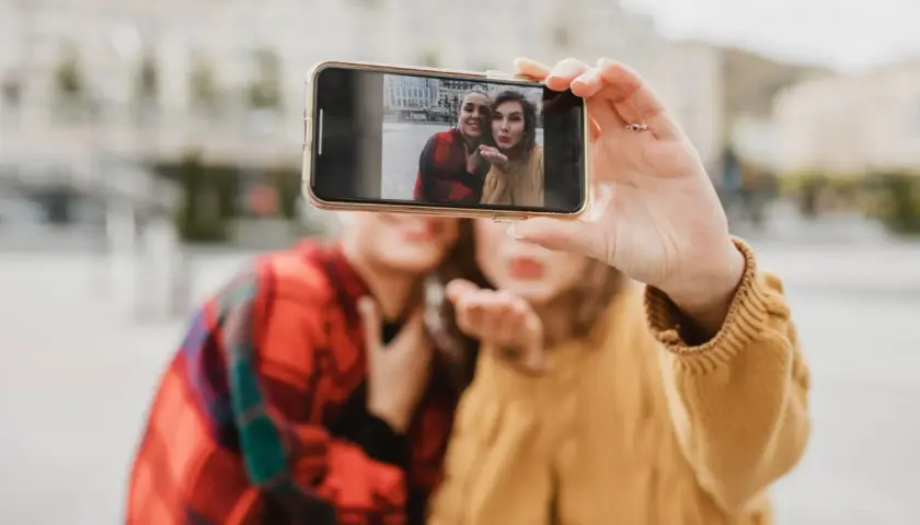 Dwie kobiety robią sobie selfie telefonem na tle miasta.