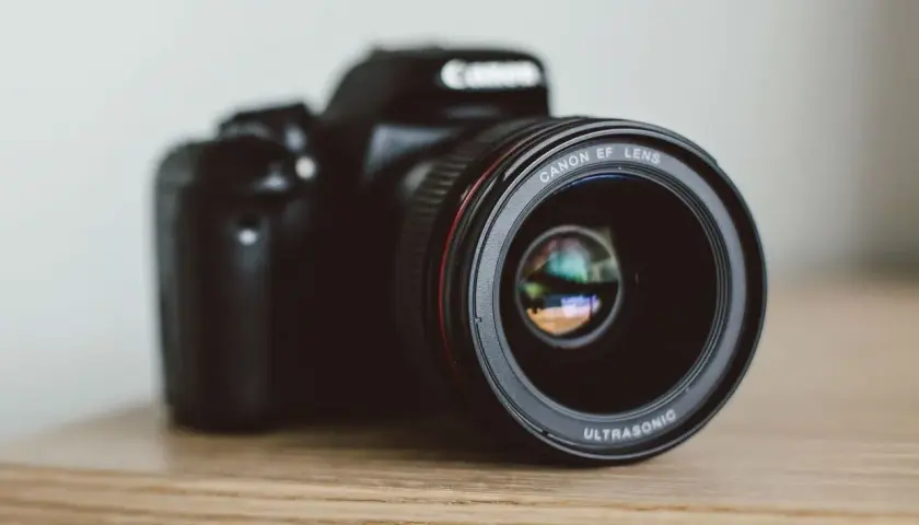 Czarna lustrzanka Canon z obiektywem EF LENS ULTRASONIC na drewnianym blacie.