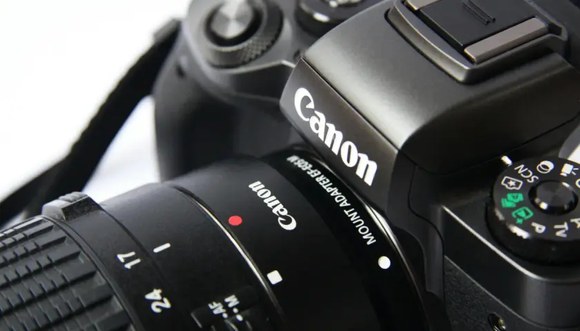 Zbliżenie na czarny aparat Canon z obiektywem, widoczne logo Canon i pokrętło trybów.
