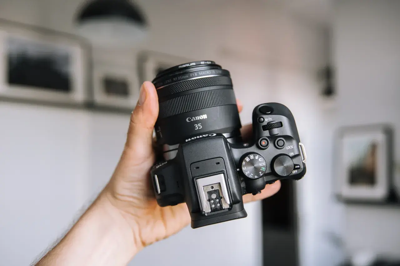 Dłoń trzyma aparat Canon z obiektywem 35mm. Zastanawiasz się, jakie aparaty fotograficzne wybrać? Ten model to świetny wybór.