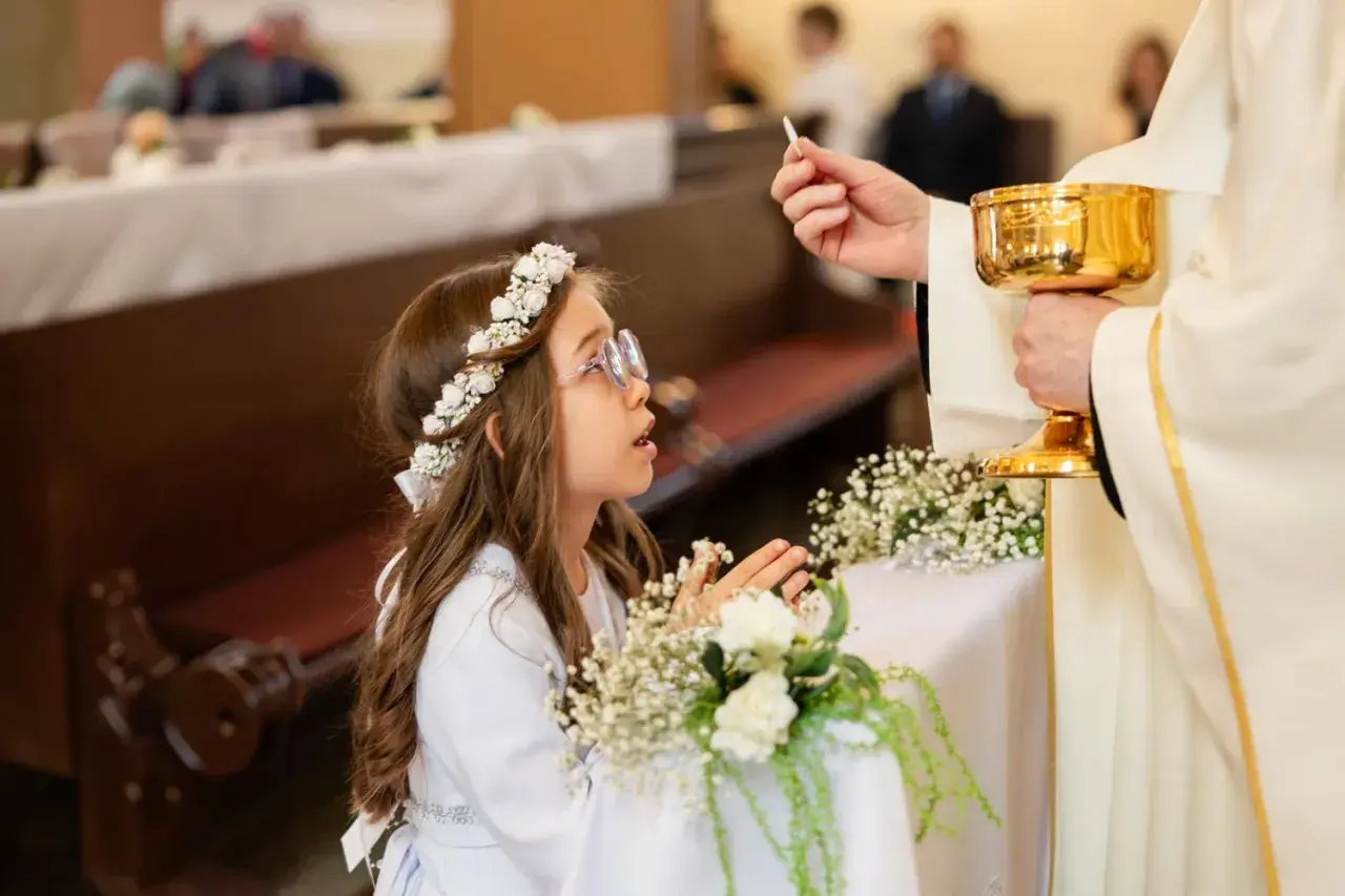 Dziewczynka w wianku przyjmuje komunię. Zastanawiasz się, ile kosztuje fotograf na komunie?