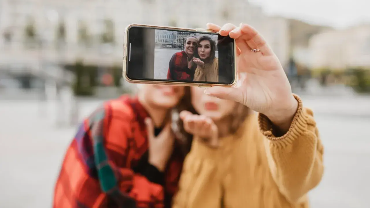 Dwie kobiety robią sobie selfie telefonem na tle miasta.