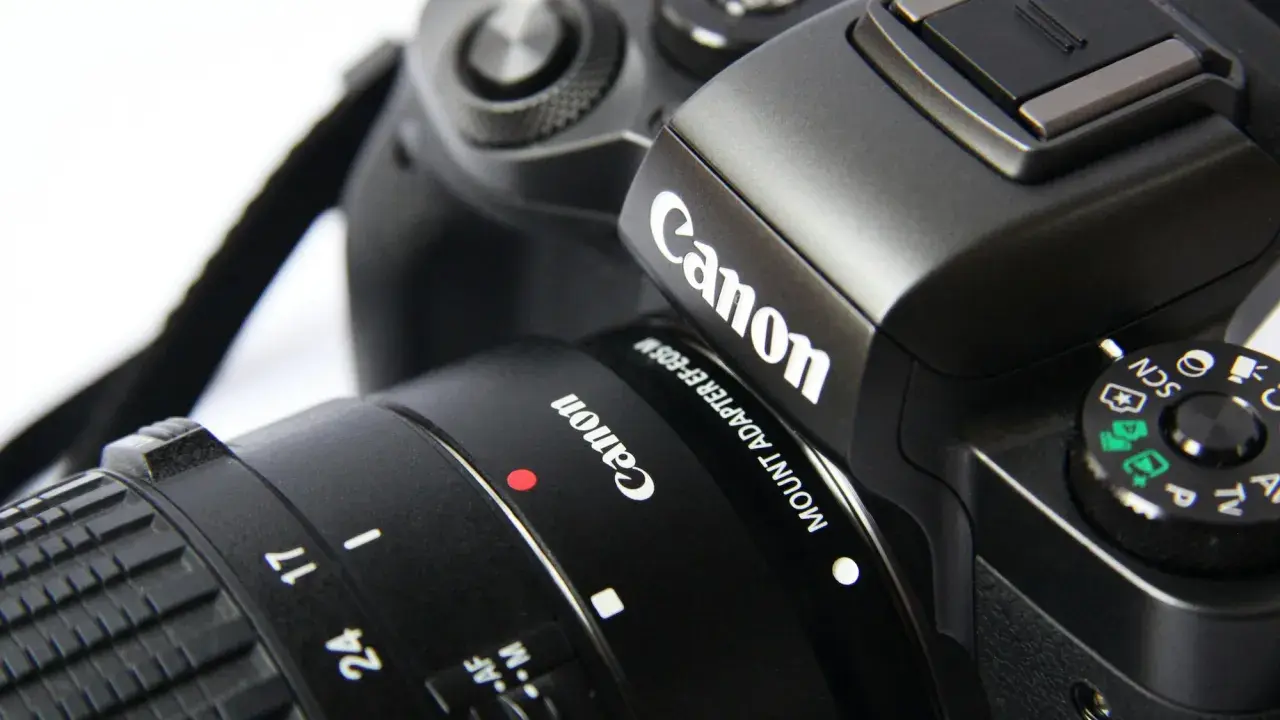 Zbliżenie na czarny aparat Canon z obiektywem, widoczne logo Canon i pokrętło trybów.