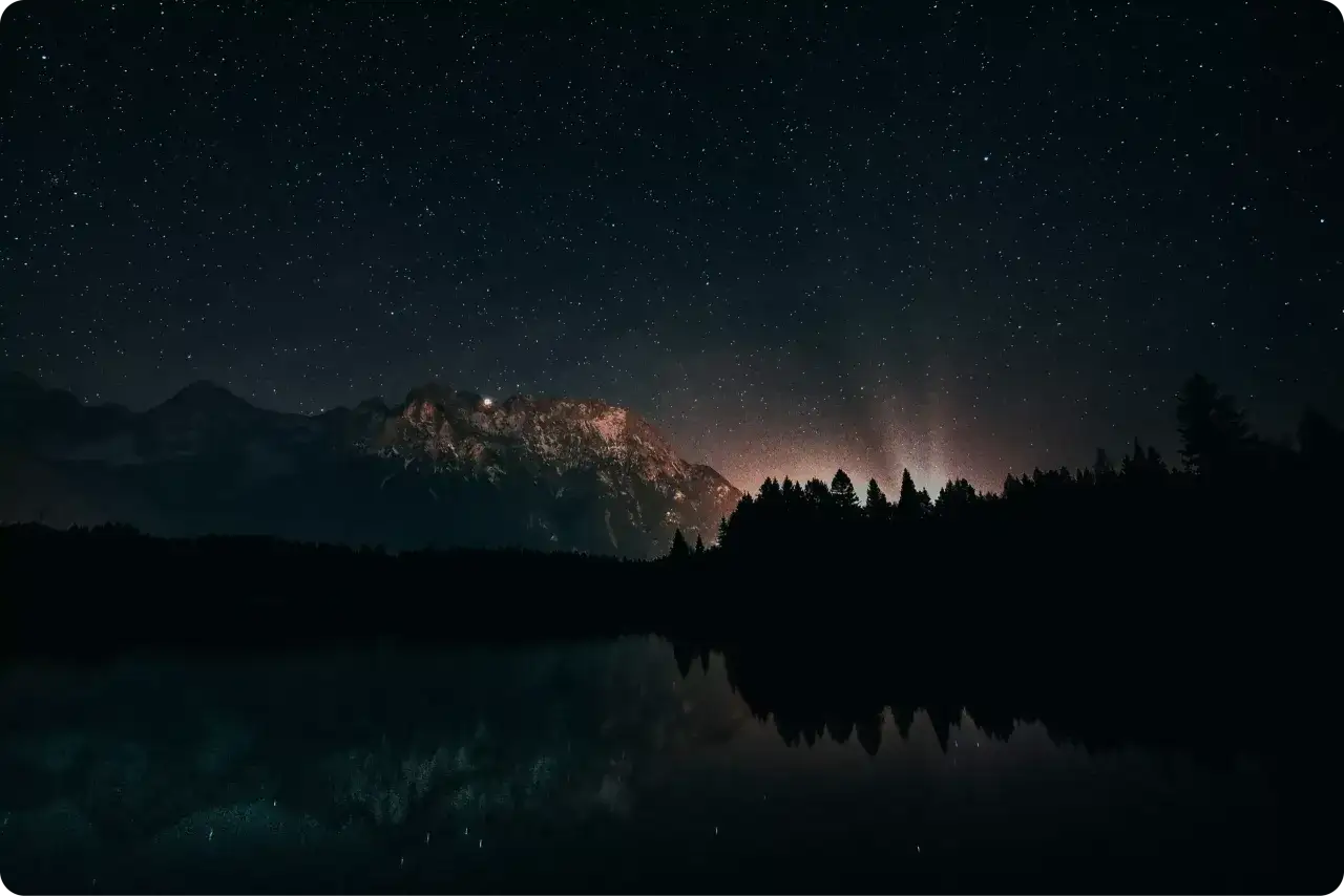 Nocne niebo pełne gwiazd nad jeziorem i górami. Dowiedz się, jak zrobić zdjęcie gwiazd iPhonem, by uchwycić takie cuda.