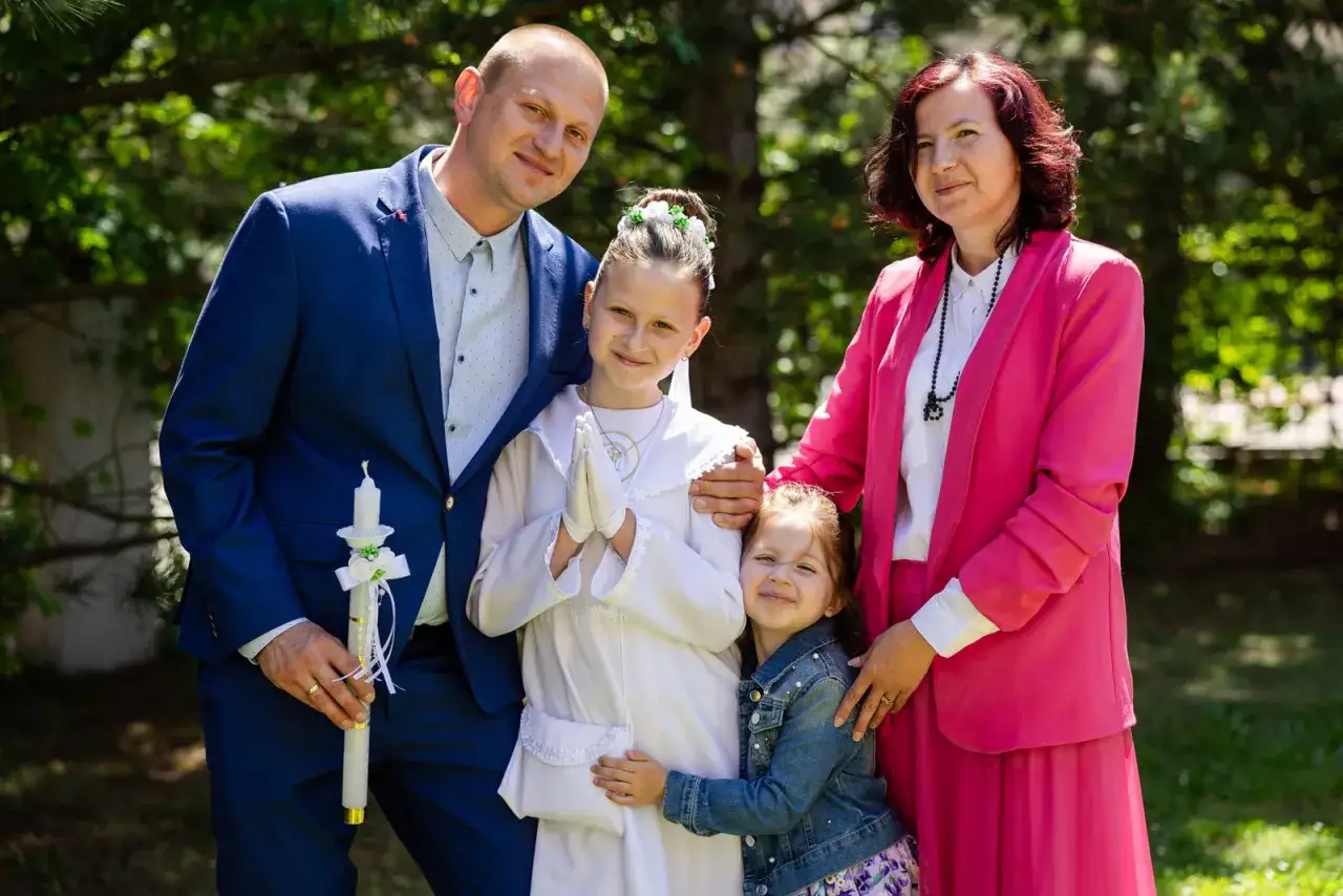 Rodzina pozuje do zdjęcia z okazji Komunii Świętej. Ojciec trzyma świecę. Zastanawiasz się, ile kosztuje fotograf na komunie?